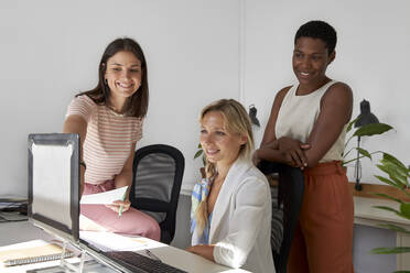 Smiling businesswoman discussing over laptop with female coworkers at office - VEGF04691