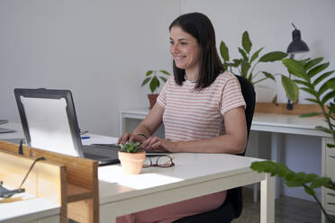 Lächelnde weibliche Fachkraft, die im Büro einen Laptop benutzt - VEGF04710