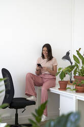 Lächelnde Geschäftsfrau, die ein Mobiltelefon auf einem Tisch im Büro benutzt - VEGF04713