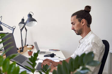 Männlicher Berufstätiger bei der Arbeit am Laptop im Büro - VEGF04728