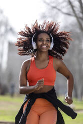 Happy female athlete with headphones running in park - RFTF00103