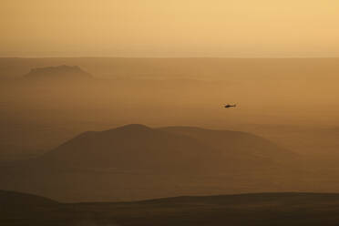 Luftaufnahme eines niedrig fliegenden Hubschraubers im Nebel mit einer schönen Landschaft im Hintergrund bei Sonnenuntergang, Grindav√≠k, Südliche Halbinsel, Island. - AAEF10347