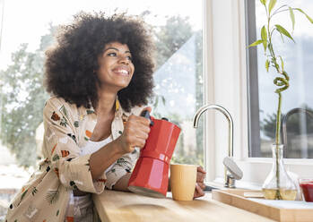 Afro woman pouring coffee from kettle in mug on kitchen counter at home - JCCMF03262