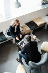 Senior businesswoman discussing over digital tablet with male colleague in cafe - JOSEF05089