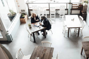 Männliche und weibliche Fachkräfte tauschen Ideen aus, während sie in einem Café über ein digitales Tablet diskutieren - JOSEF05092