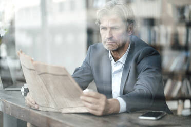Älterer Geschäftsmann, der in einem Café sitzt und Zeitung liest, gesehen durch ein Glasfenster - JOSEF05104