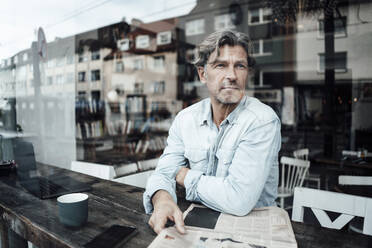 Mature man sitting with newspaper in cafe seen through glass window - JOSEF05124