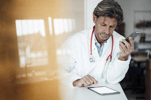 Männlicher Angestellter im Gesundheitswesen verwendet ein digitales Tablet, während er sich in einer Klinik auf den Schreibtisch stützt - JOSEF05142