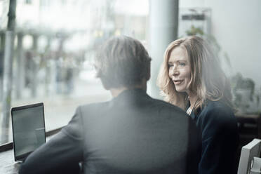 Senior businesswoman discussing with male colleague while sitting in cafe - JOSEF05157