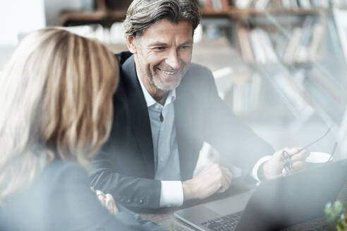 Smiling mature businessman discussing with female colleague over laptop sitting in cafe - JOSEF05163