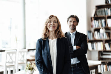 Smiling senior blond businesswoman standing with male colleague in cafe - JOSEF05164