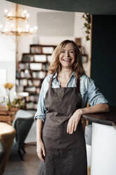 Happy female cafe owner wearing apron while standing in coffee shop - JOSEF05168