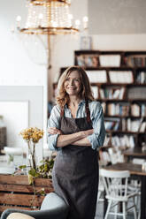 Smiling female coffee shop owner looking away while standing with arms crossed - JOSEF05171