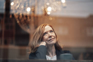 Thoughtful female professional with blond hair seen through glass window - JOSEF05187