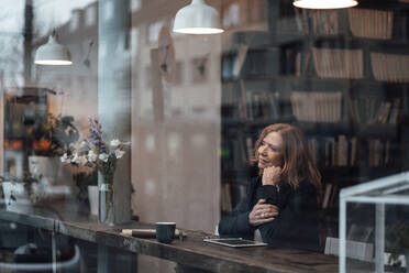 Thoughtful businesswoman sitting in cafe looking through glass window - JOSEF05190