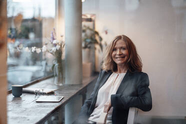 Smiling senior female professional with blond hair sitting in cafe - JOSEF05191