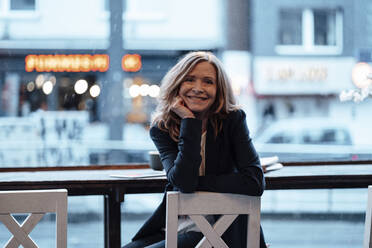 Smiling businesswoman leaning on chair while sitting in cafe - JOSEF05196