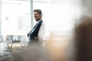 Smiling male professional standing with arms crossed in cafe - JOSEF05199