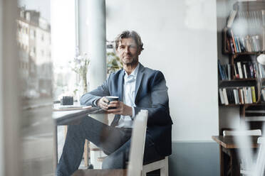 Businessman holding coffee cup while sitting in cafe - JOSEF05202