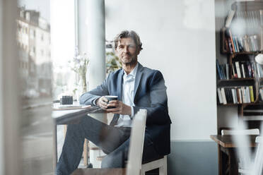 Geschäftsmann hält Kaffeetasse, während er in einem Cafe sitzt - JOSEF05202