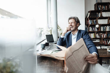 Männlicher Profi lacht, während er mit einer Zeitung in einem Café sitzt - JOSEF05207