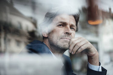 Mature businessman with gray hair and stubble seen through glass window - JOSEF05208
