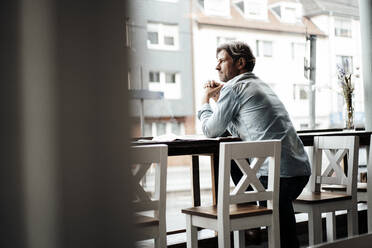 Mature man with hands clasped leaning on table standing in cafe - JOSEF05211