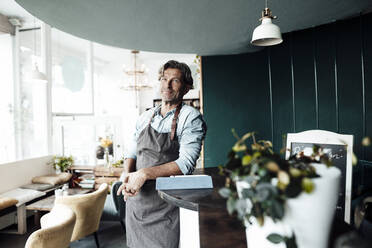 Mature male cafe owner standing while leaning on table - JOSEF05219