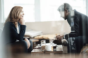 Ältere weibliche Fachkraft mit Hand am Kinn, die einen männlichen Kollegen bei einer Diskussion im Café ansieht - JOSEF05226