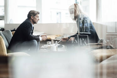 Mature businessman looking at female colleague discussing while sitting together in cafe - JOSEF05229