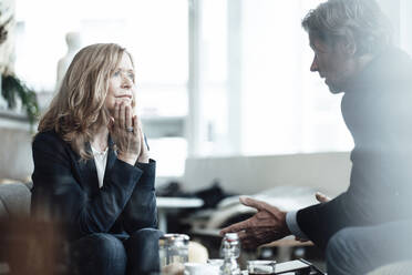 Blond senior female professional looking at male colleague sharing ideas while discussing in cafe - JOSEF05234