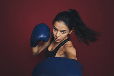 Confident sportswoman boxing against maroon background - OYF00408