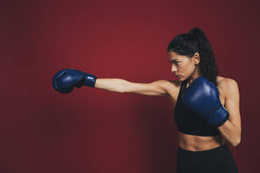 Confident female athlete practicing punches in front of maroon wall - OYF00409