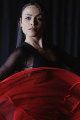Junge Frau mit Make-up in roter und schwarzer Kleidung, die einen traditionellen spanischen Tanz aufführt und dabei in die Kamera schaut - ADSF27650