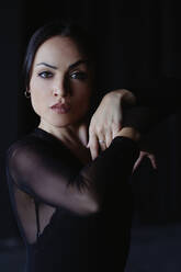 Junge anmutige Frau in schwarzer Kleidung tanzt Flamenco mit erhobenen Armen und schaut in die Kamera - ADSF27657