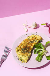 Leckeres Omelett auf einem Teller gegen frische Petersilienzweige und rote Zwiebel mit Knoblauchzehen auf rosa Hintergrund - ADSF27670