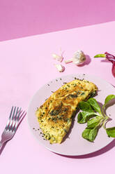 Tasty omelette on plate against fresh parsley sprigs and red onion with garlic cloves on pink background - ADSF27670