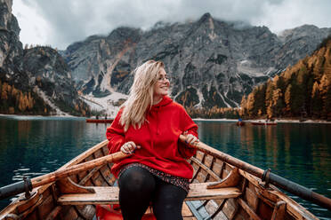 Lächelnde Frau auf Holzboot mit Paddeln schwimmt auf türkisfarbenen Wasser der ruhigen See auf dem Hintergrund der majestätischen Landschaft der Hochland in Dolomiten in Italien Alpen - ADSF27691