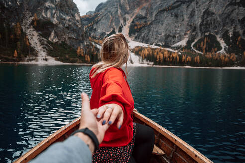 Rückenansicht von unerkennbaren blonde Frau hält Hände mit Ernte Mann auf hölzernen Boot mit Paddeln schwimmend auf türkisfarbenem Wasser der ruhigen See auf dem Hintergrund der majestätischen Landschaft der Hochland in Dolomiten in Italien Alpen - ADSF27692