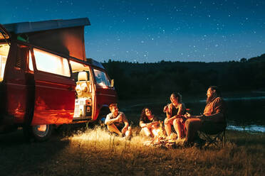 Fröhliche Gruppe von Freunden haben Spaß Camping in der Nähe von See und van während sternenklare Nacht - ADSF27696