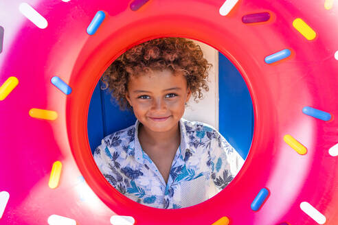 Curly haired boy holding multi colored inflatable doughnut - DLTSF02057