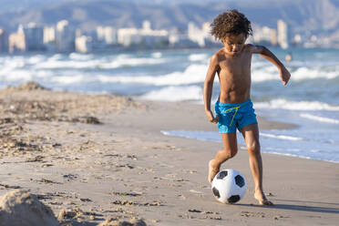 Shirtless boy playing with soccer ball at beach - DLTSF02059