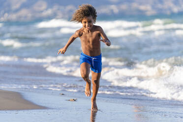 Cheerful boy running on coastline at beach - DLTSF02061