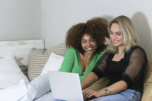 Lächelnde Freundinnen, die zu Hause einen Laptop benutzen - PNAF02052