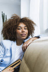 Junge Frau mit Buch sitzt zu Hause auf dem Sofa - PNAF02104