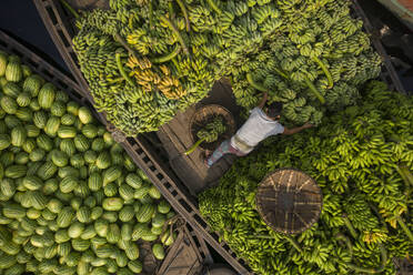 Aerial view of a person unloading fresh watermelons and banana fruits from a wooden boat in Buriganga river in Dhaka, Bangladesh. - AAEF10491