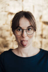 Young woman wearing eyeglasses sticking out tongue - JOSEF05244