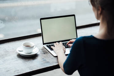 Young businesswoman typing on laptop sitting at table in cafe - JOSEF05260