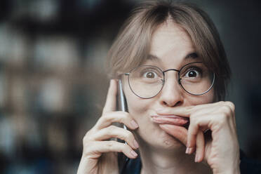 Female freelancer making face while talking on mobile phone in cafe - JOSEF05264