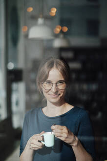 Smiling young woman holding coffee cup in cafe - JOSEF05277